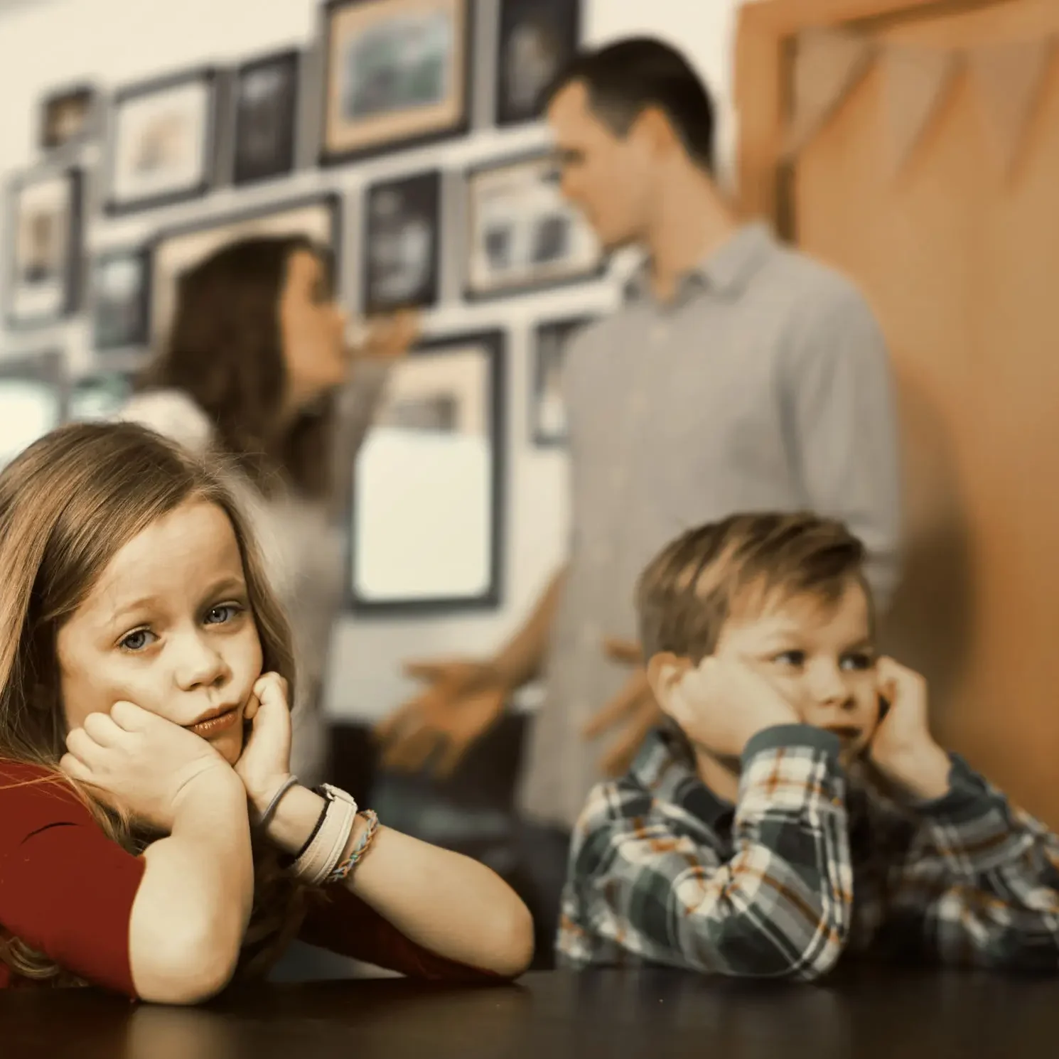 Two children sitting at a table with adults blurred in background.