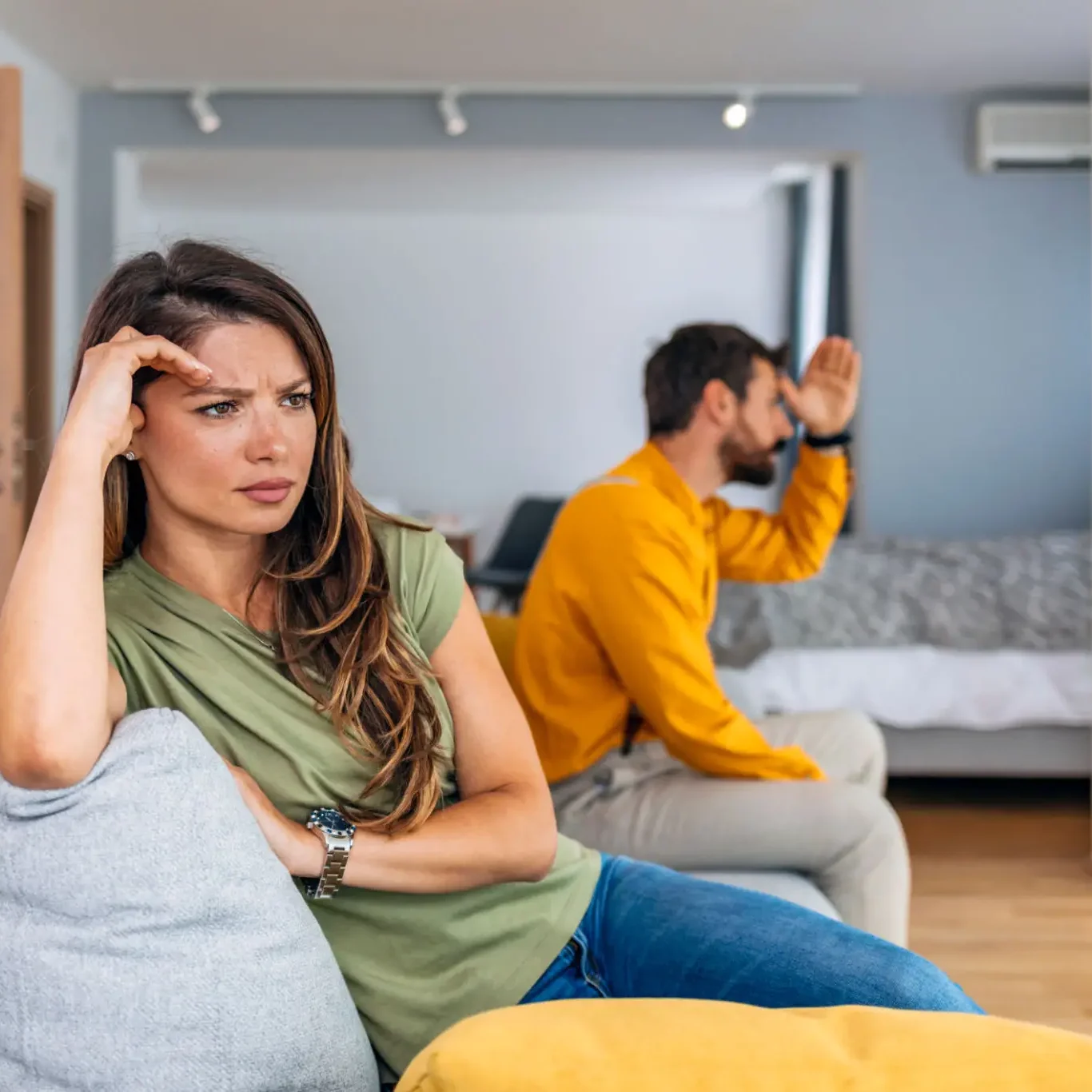 A couple sitting separately looking upset and stressed at home.